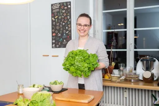 Storyteller steht in der Küche und hält lächelnd einen Kopfsalat.