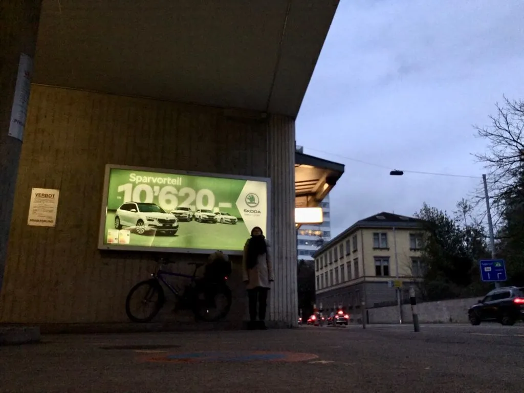 Storyteller steht vor einem grossen, beleuchteten Werbeplakat für Autos.