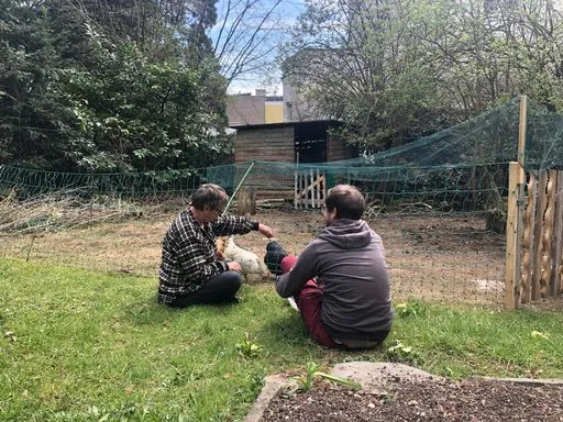 zwei Personen sitzen im sonnigen Garten bei den Hühnern