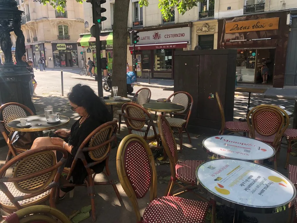Ein Café mit kleinen Tischen im Schatten der Bäume.