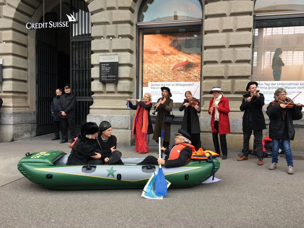 Menschen an einer aktivistischen Aktion in einem Schlauchboot vor einer Bank.