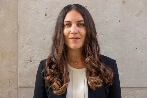 Person mit einem Blazer steht vor grauer Wand.