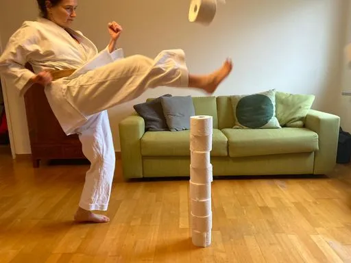 Storyteller in Karate-Kleidung kickt in einen Turm aufgestapelter WC-Rollen.