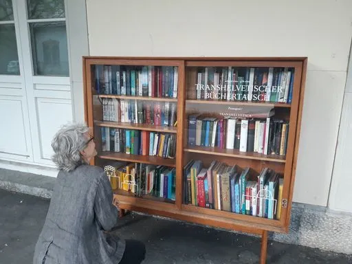 Storyteller kniet vor einem Bücherregal, welches draussen vor einem Gebäude steht.