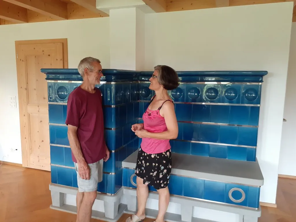 Frau und Mann stehen vor einem blauem Kachelofen.