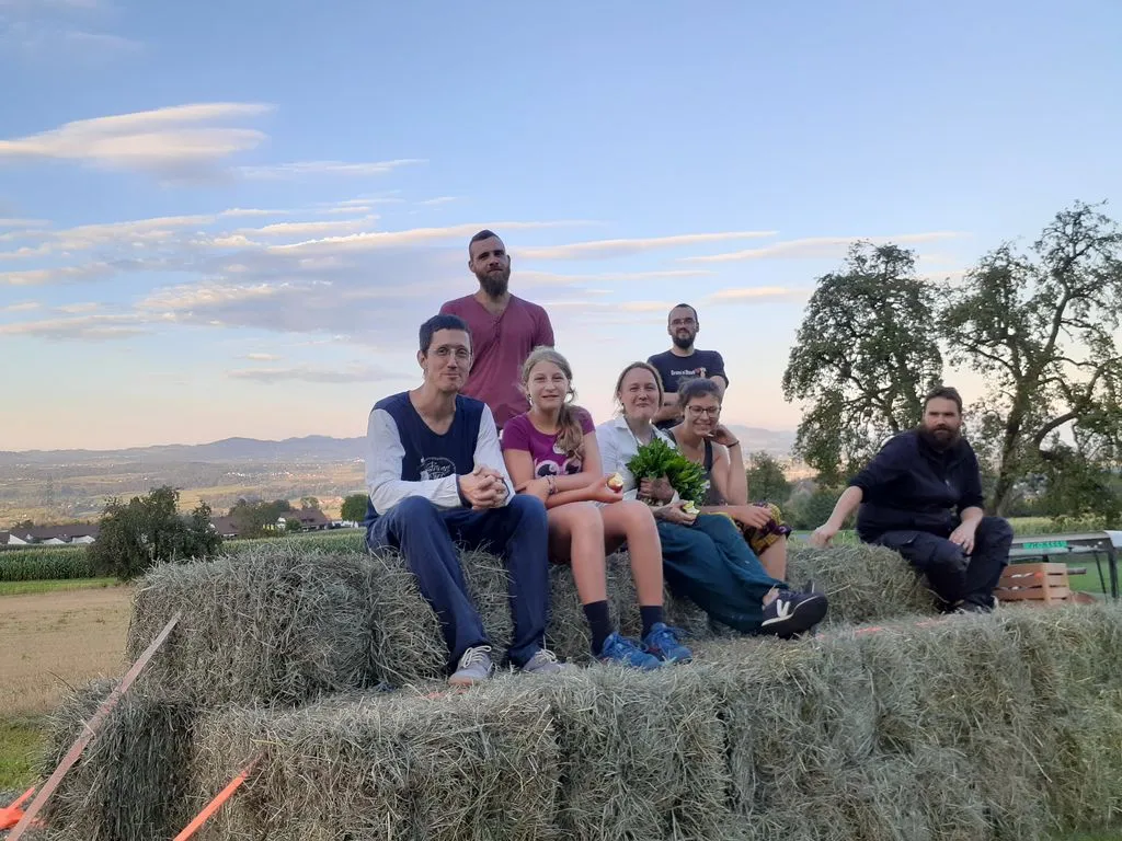 Erwachsene und Kinder sitzen auf einem Stapel Heuballen auf einem Feld.